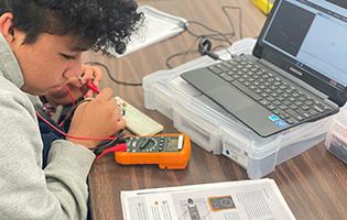 Young student studies instructions while holding wires 