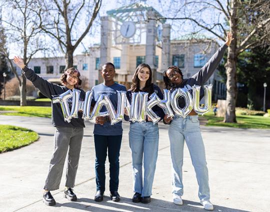 group holds balloons that spell "thank you"